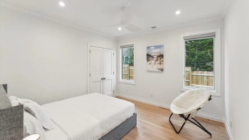 A bright bedroom with a bed, two windows, and a lounge chair.
