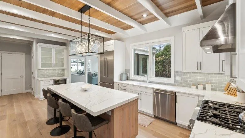 A bright kitchen with a large island, stainless steel appliances, and wood ceiling beams.