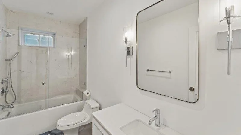 A bright bathroom with a bathtub, toilet, and wide mirror.