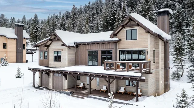 Una casa cubierta de nieve con un balcón de madera está entre árboles de hoja perenne.