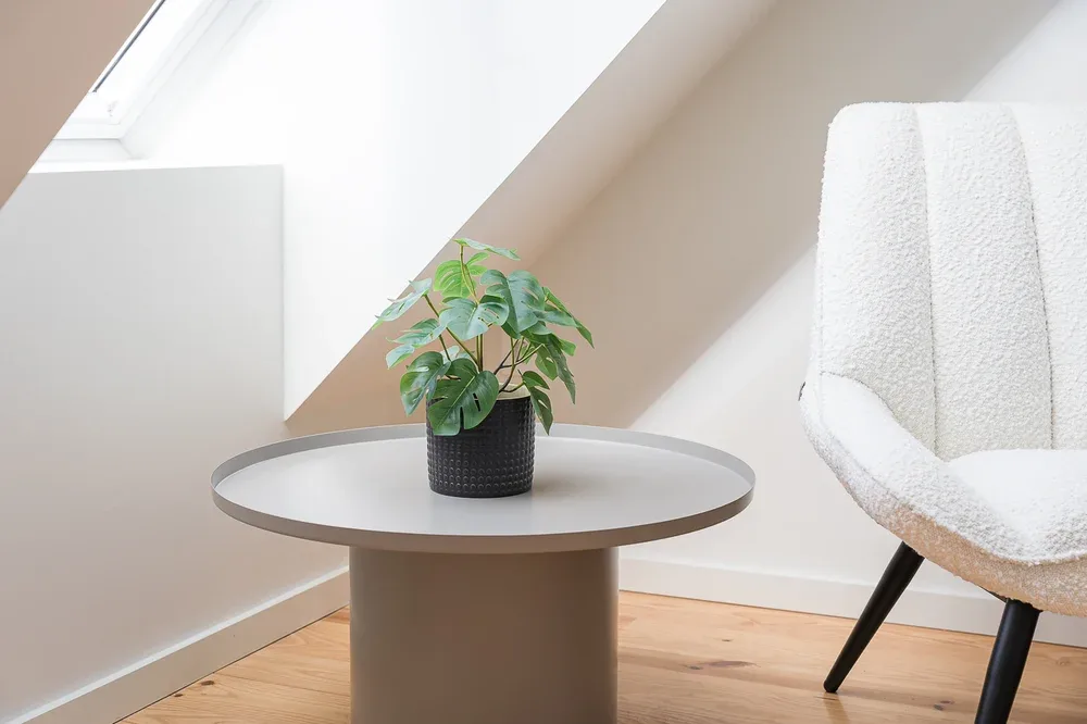 A bright sitting area has a round table with a potted plant beside a chair.