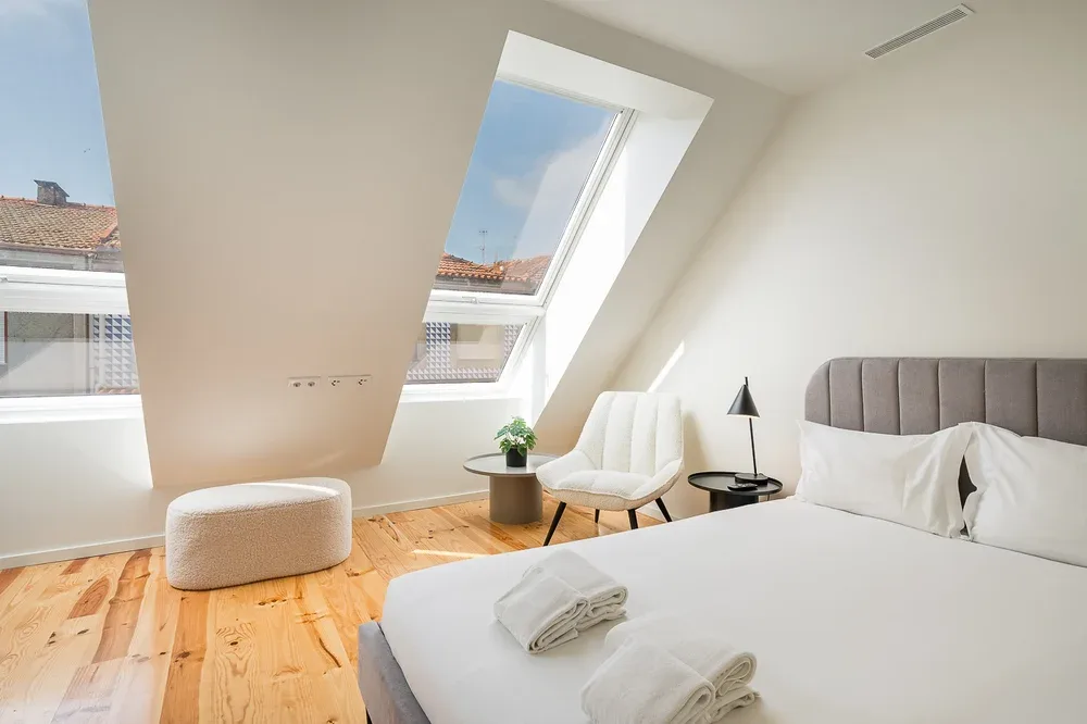 Un dormitorio abuhardillado luminoso con cama, asientos y grandes claraboyas.