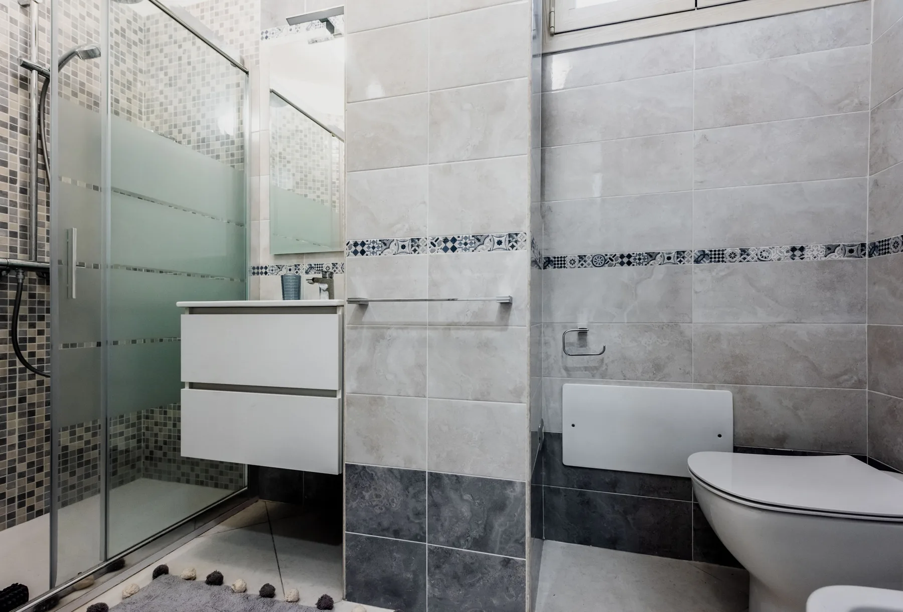 A tiled bathroom with a glass shower, vanity, and toilet.