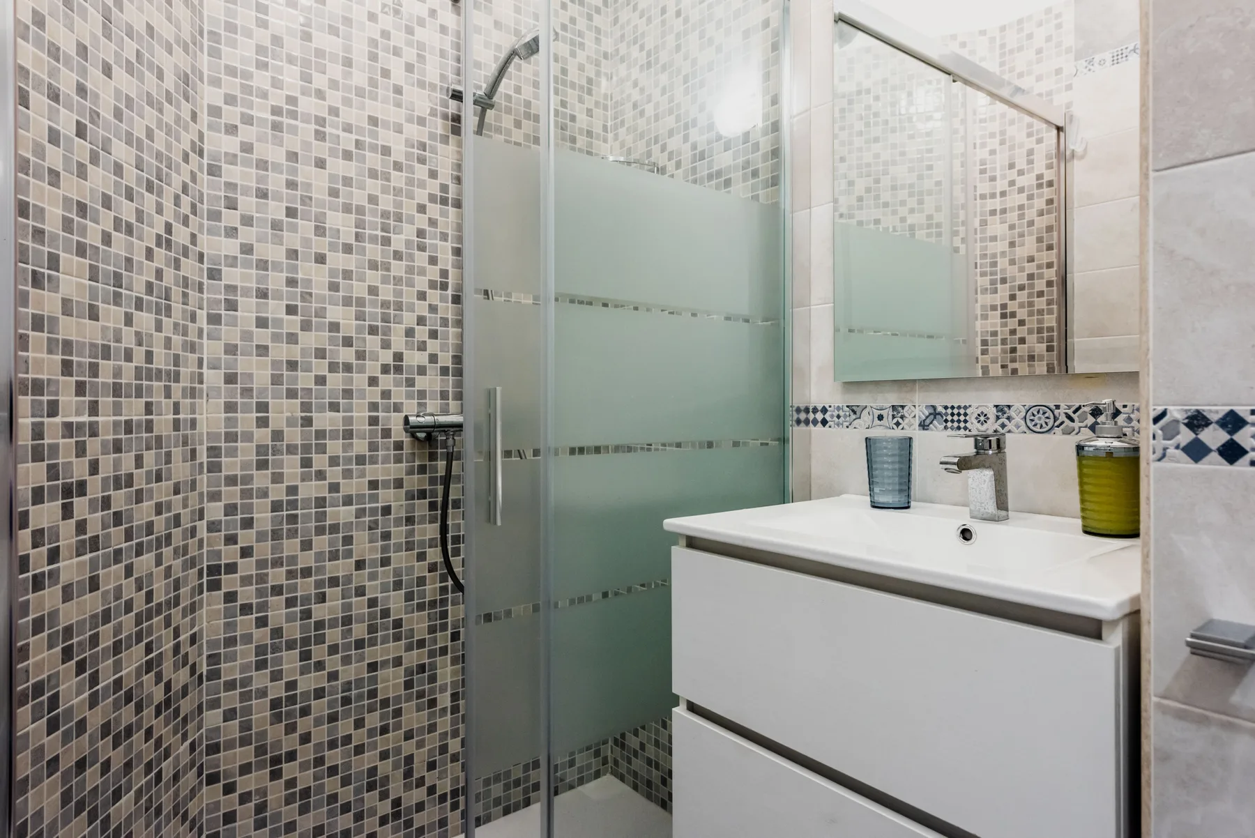 A tiled bathroom with a glass shower and white vanity.