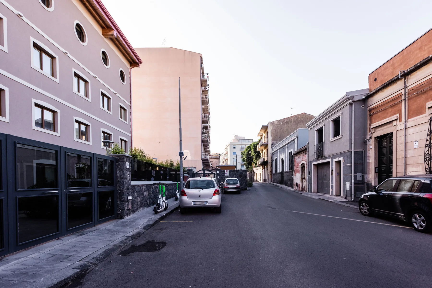 A quiet urban street lined with low-rise buildings and parked cars.