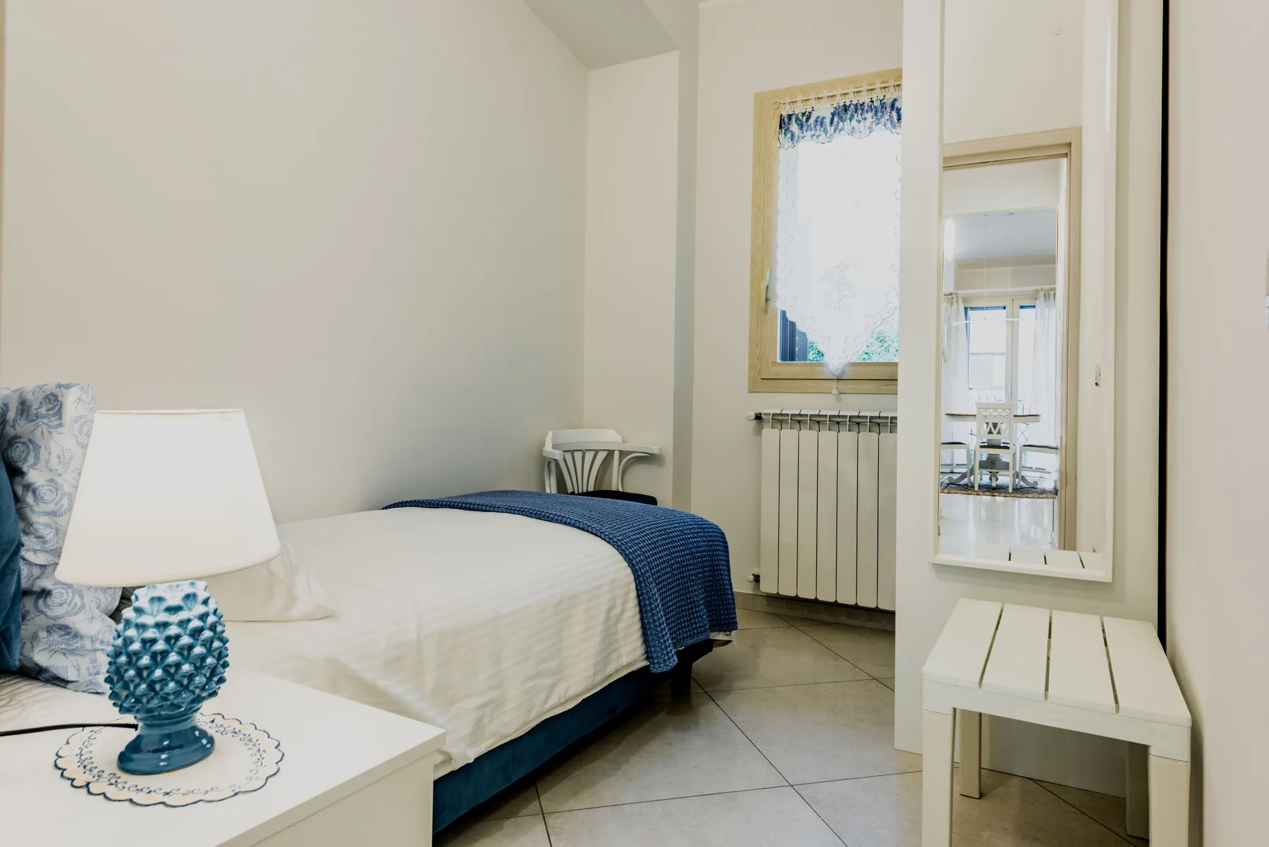 A bedroom with a bed covered by white bedding and a blue blanket.