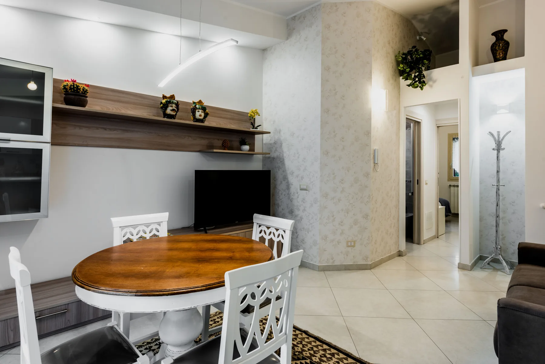 A dining area with a round wooden table beside a television and hallway.