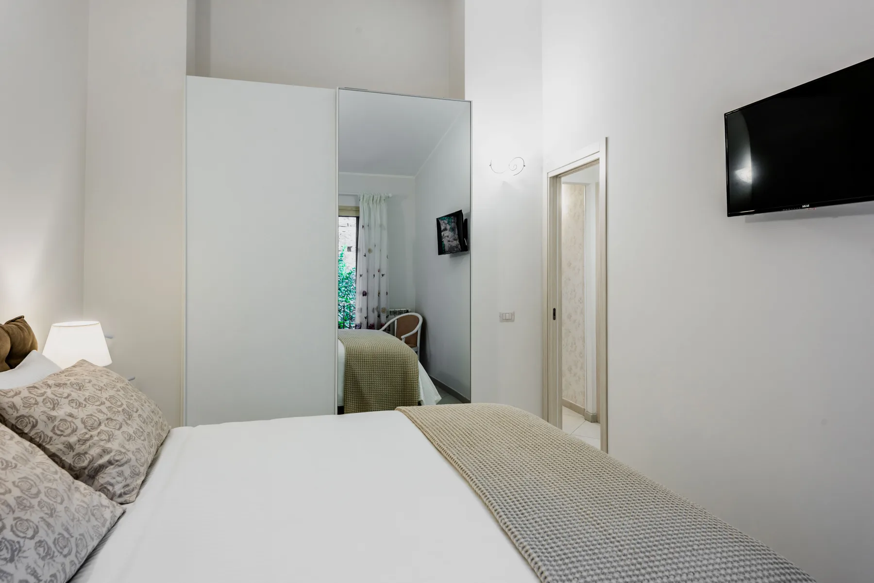 A bedroom with a neatly made bed and a wall-mounted television.