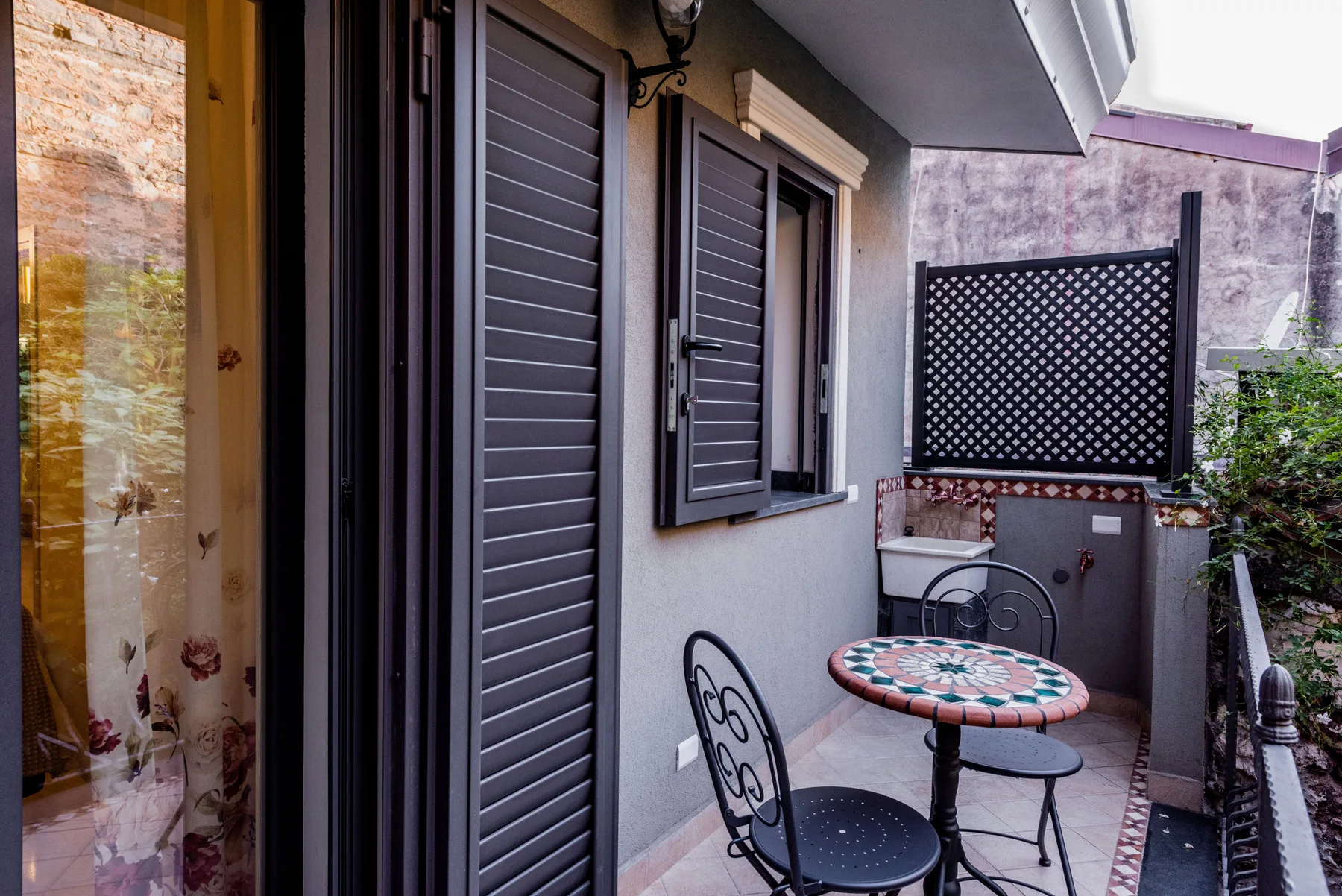Un pequeño patio exterior con asientos metálicos y una mesa redonda estampada.
