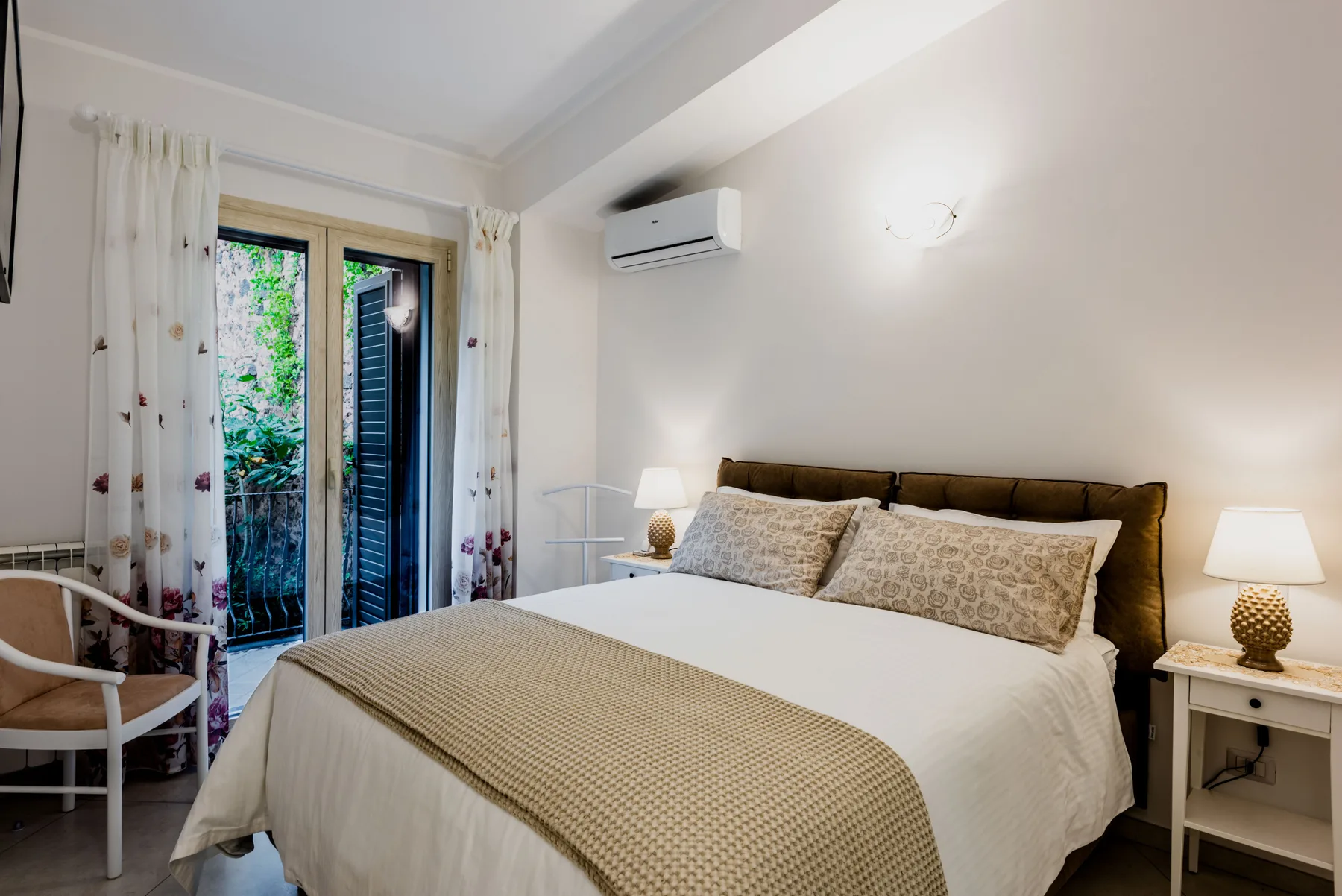 A bedroom with a neatly made bed and glass doors opening to greenery.