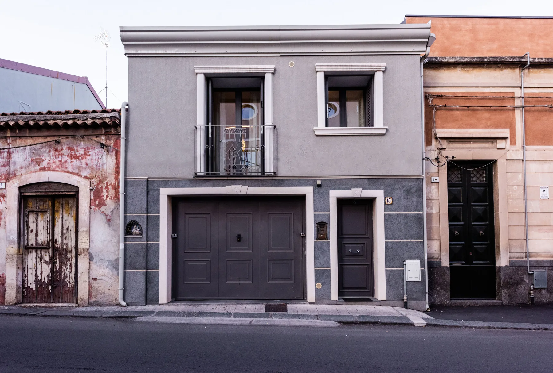 Un edificio gris con puertas y ventanas oscuras se encuentra entre fachadas antiguas.