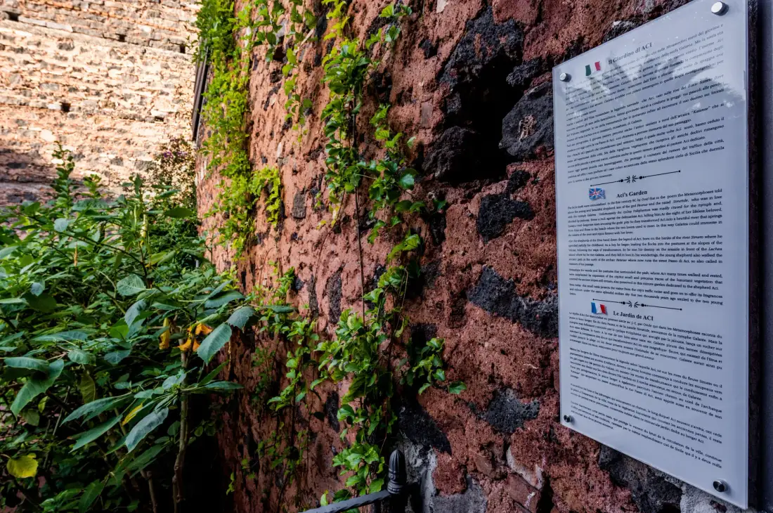 A leafy outdoor passage runs alongside a weathered brick wall with an informational sign.
