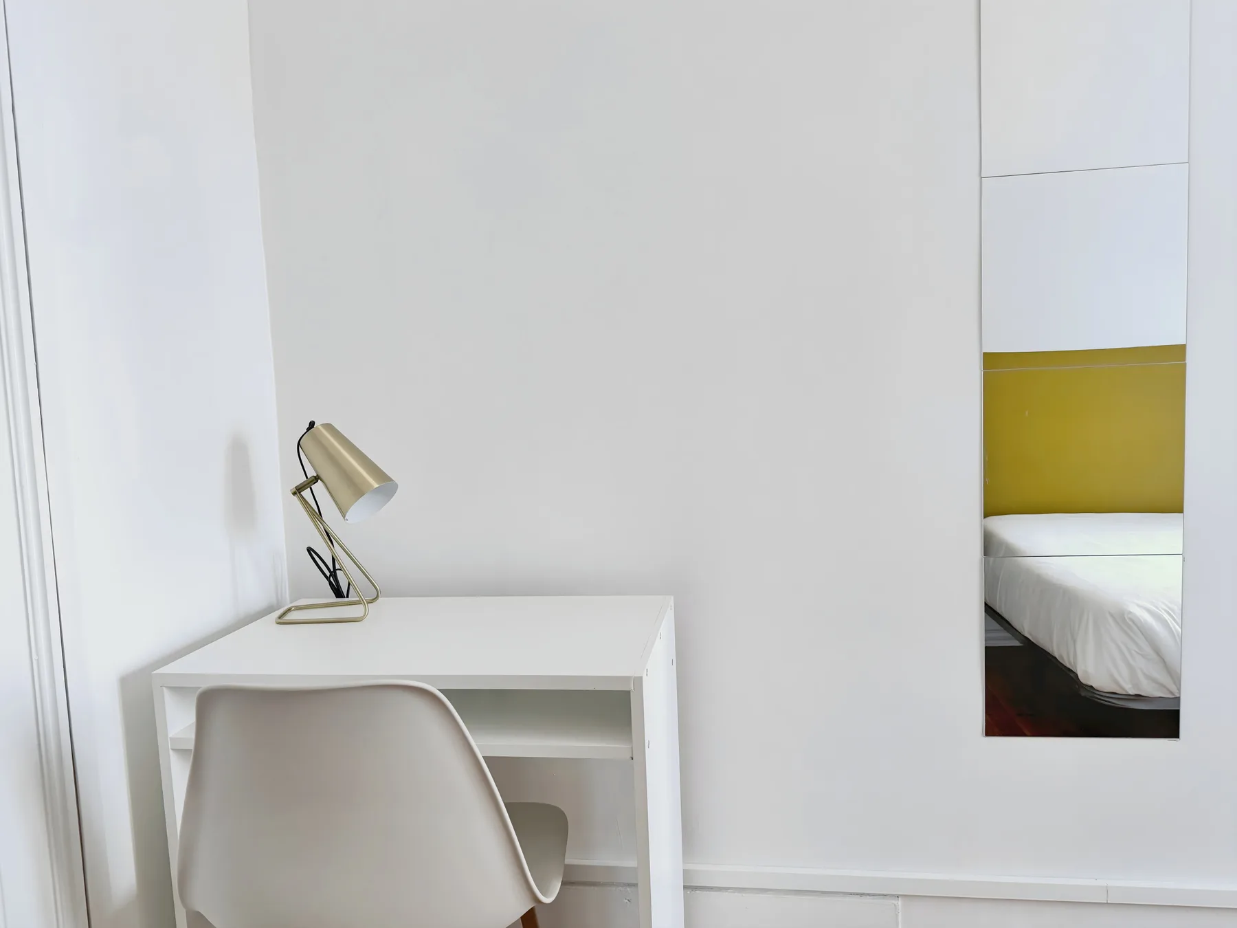 A white desk and chair sit beside a wall mirror in a bright bedroom.