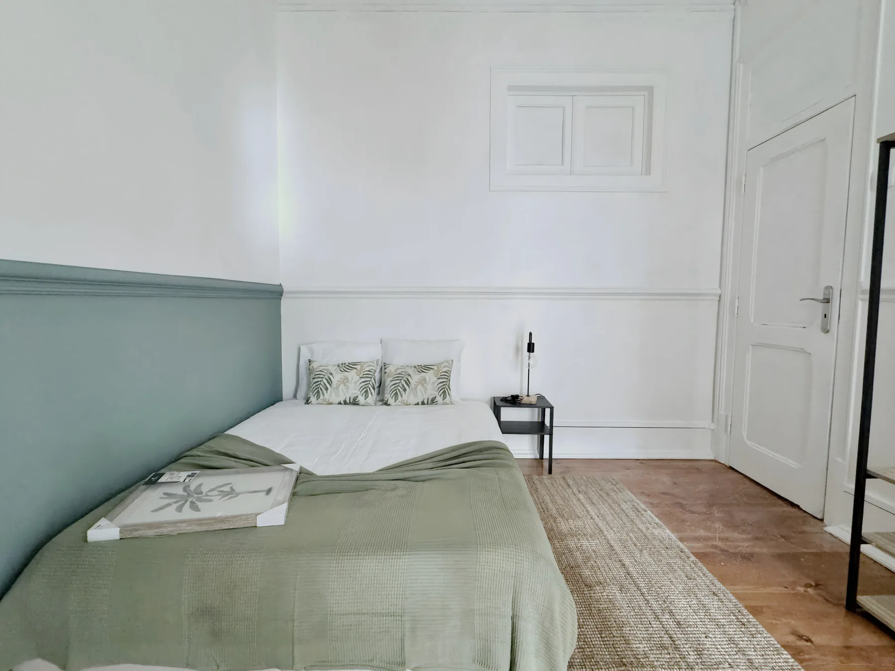 A bedroom with a bed, pale green bedding, and a woven rug.
