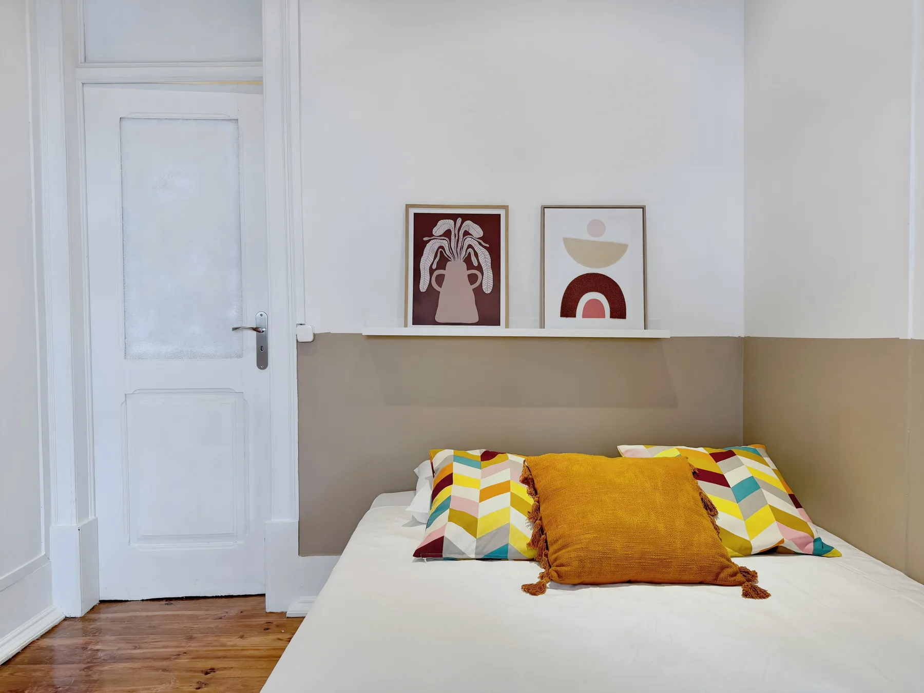 A bedroom with a bed, colorful pillows, and framed artwork above a shelf.