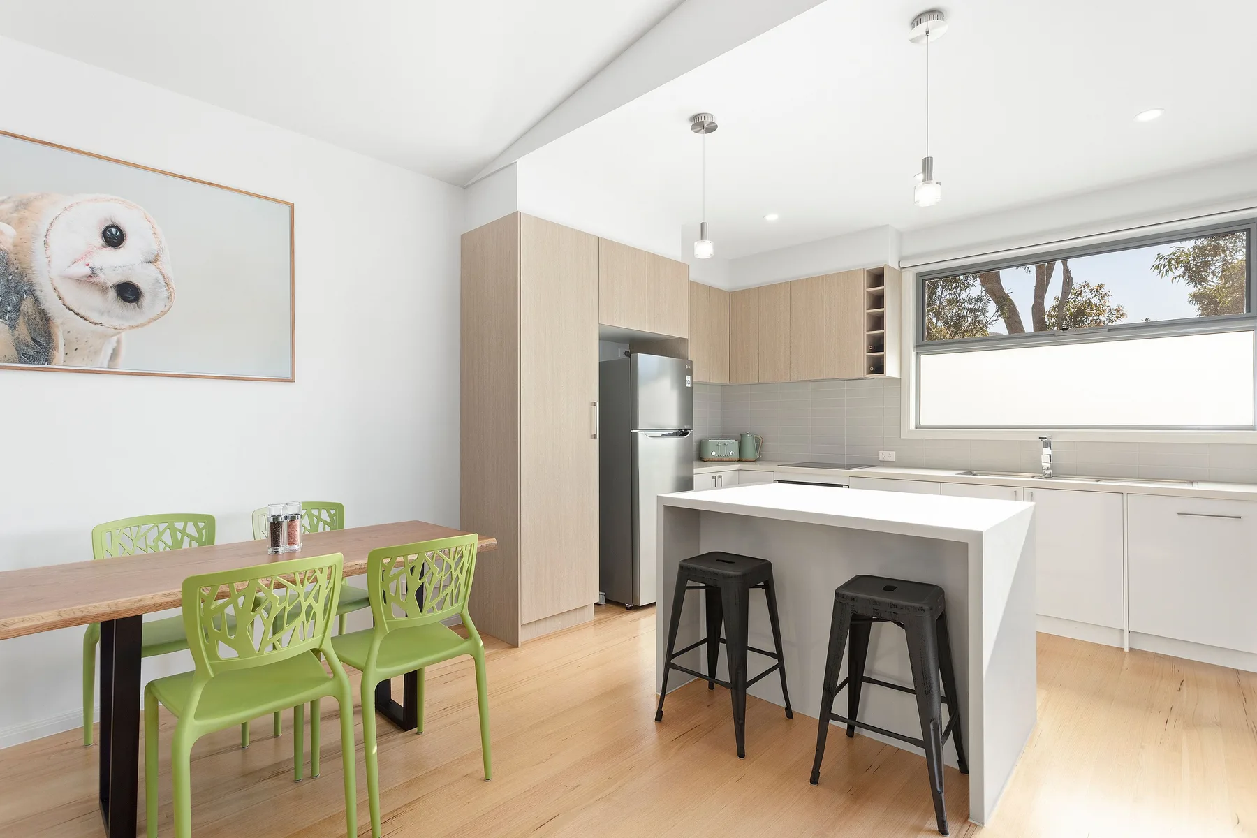 A bright kitchen and dining area with a white island and green seating.