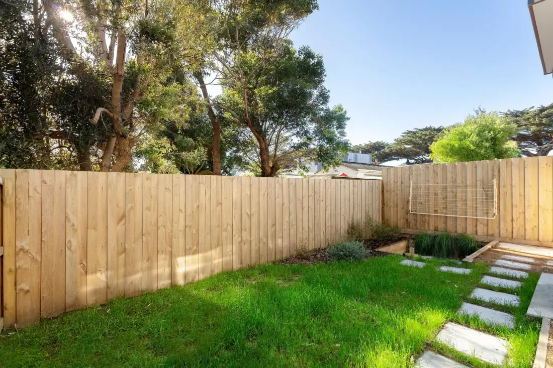 A fenced garden with green lawn, trees, and a stepping-stone path.
