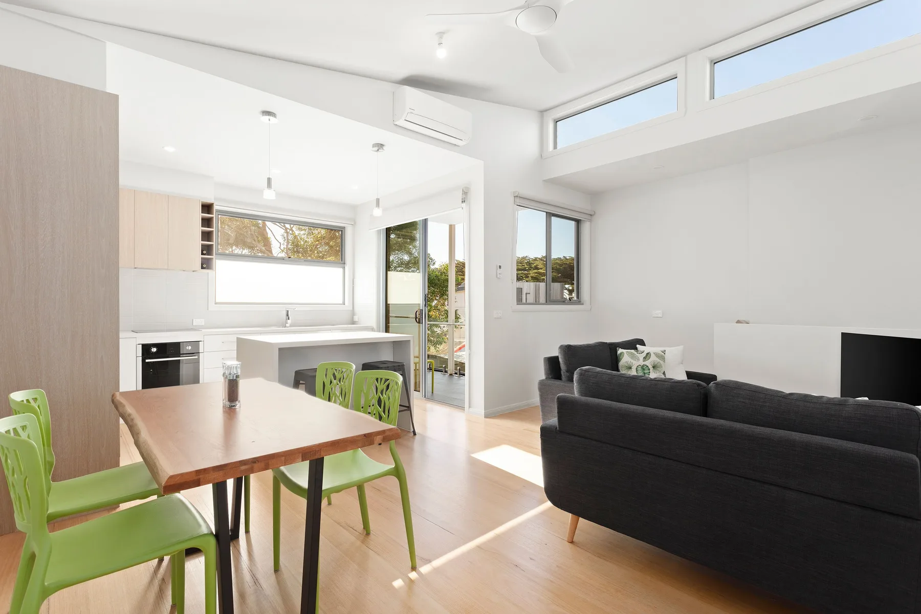 A bright open-plan living and dining area with a kitchen and green seating.