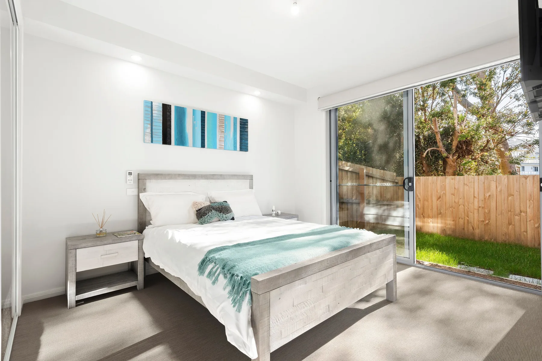 Un dormitorio luminoso con una cama junto a puertas corredizas de vidrio que dan al jardín.
