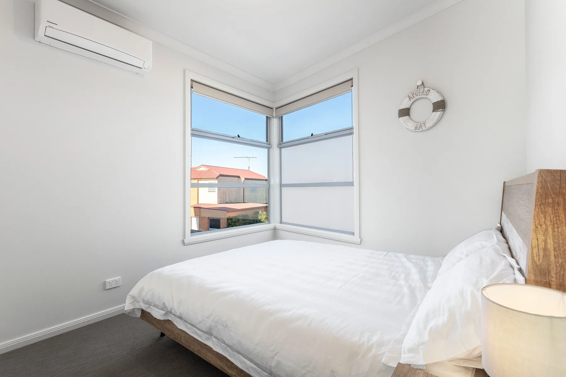 A bright bedroom with a bed beside corner windows.