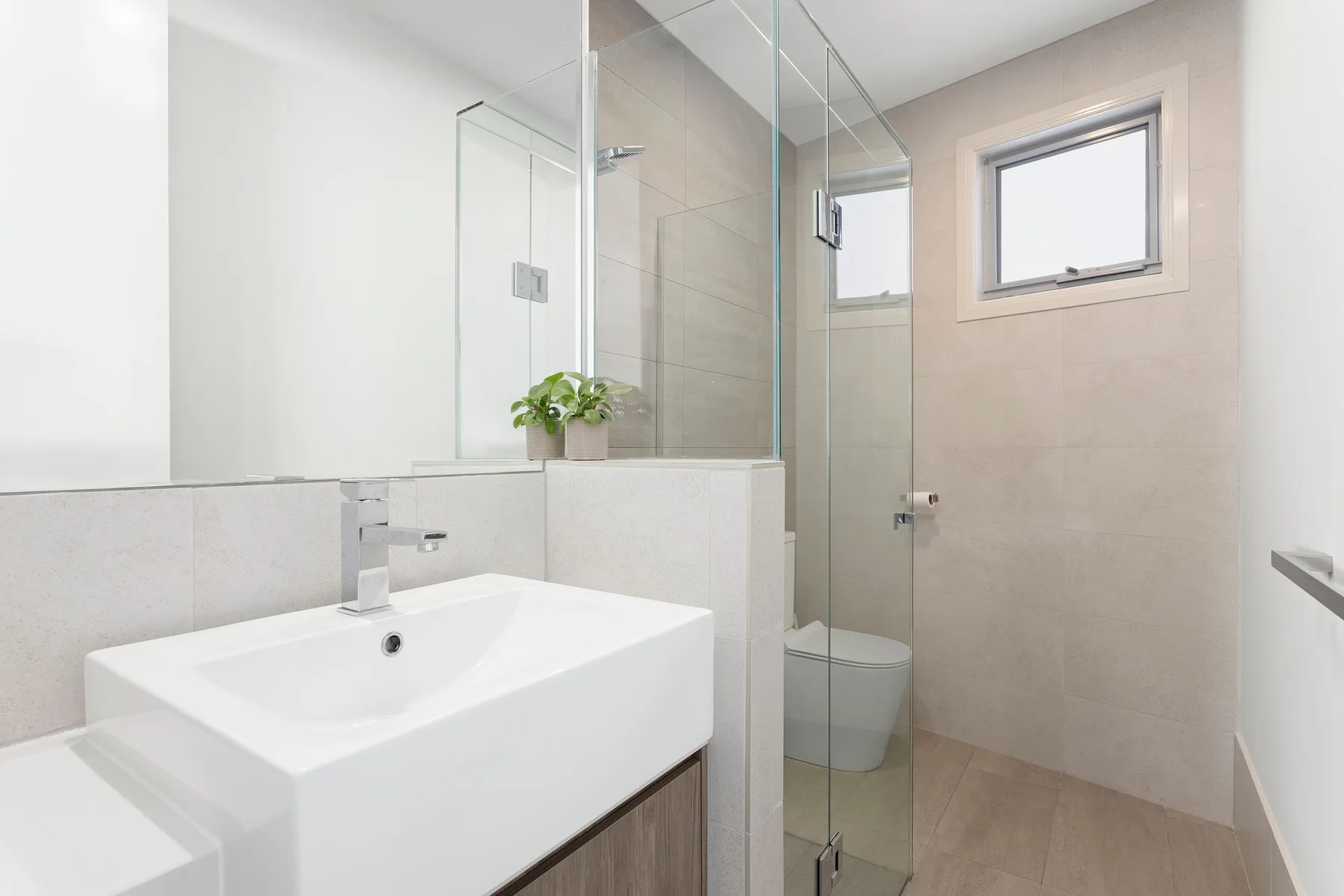 A modern bathroom with a white sink and glass shower.