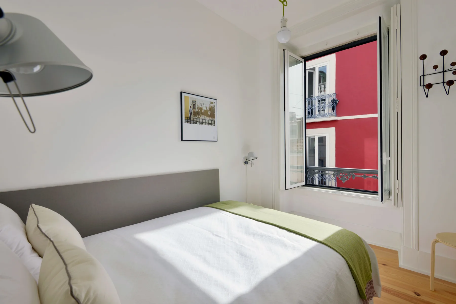 A bedroom with a bed beside an open window overlooking a red building.