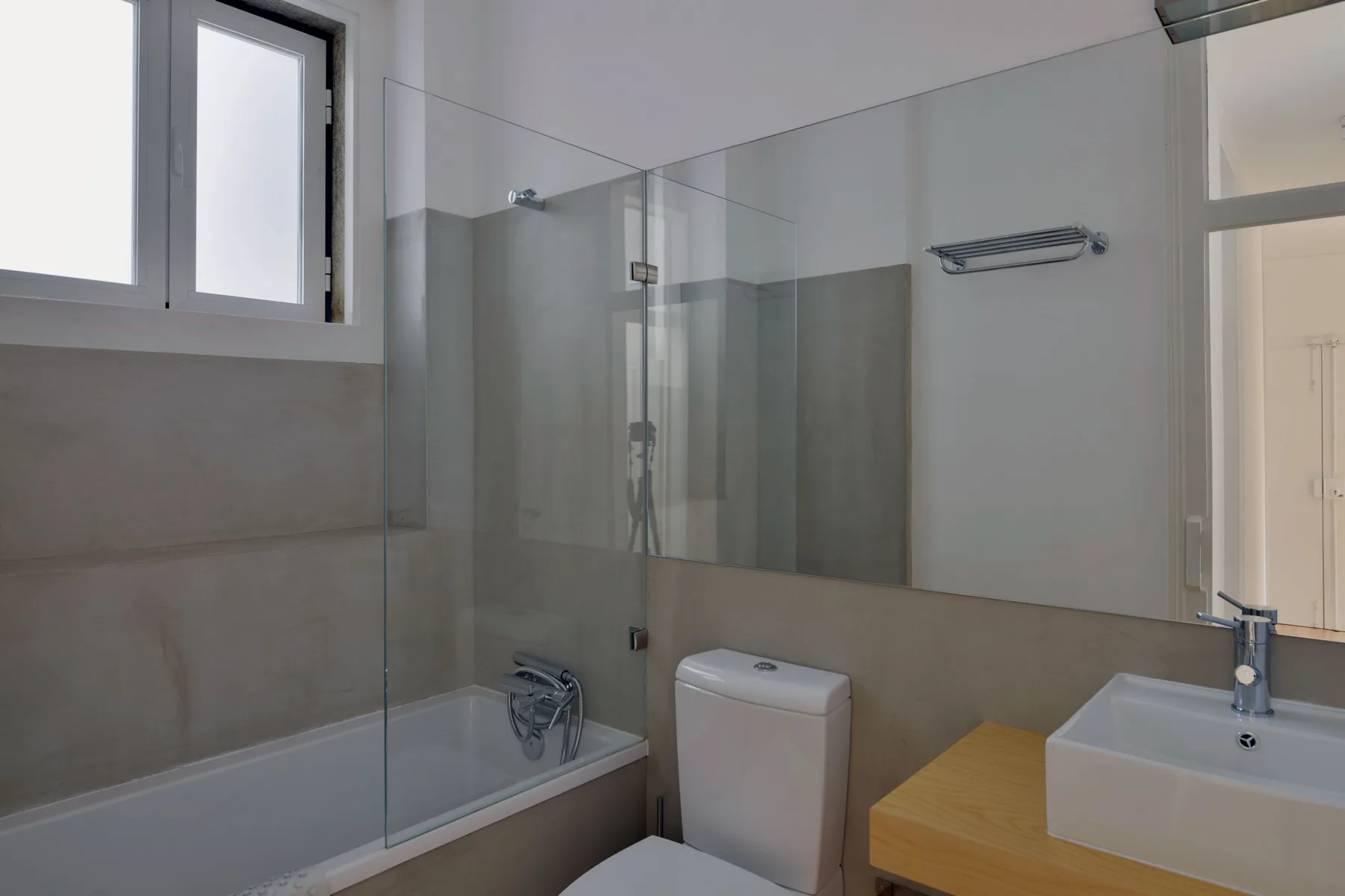 A bright bathroom with a bathtub, glass shower screen, and sink.
