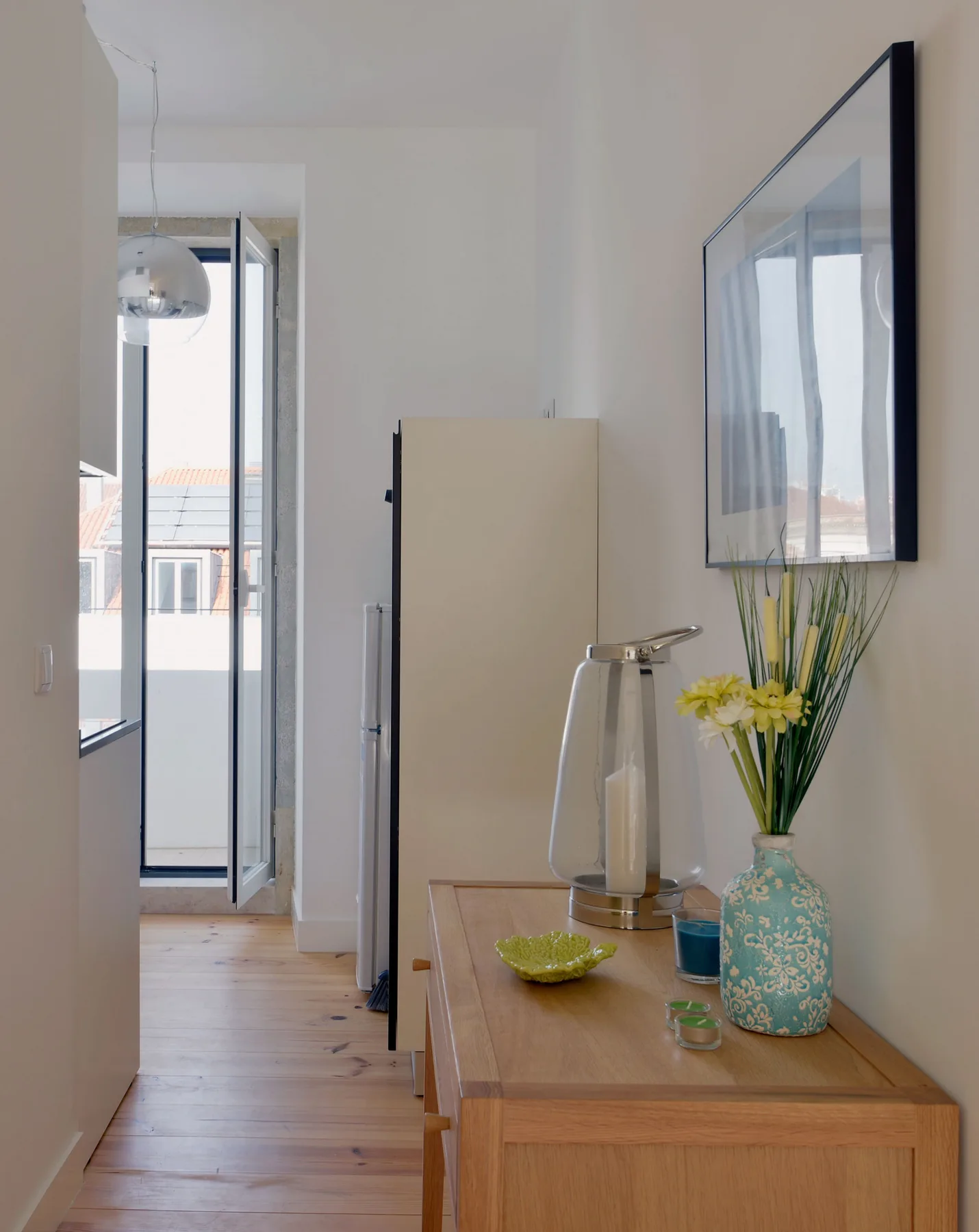 A bright hallway with a wooden console table, flowers, and a framed picture.