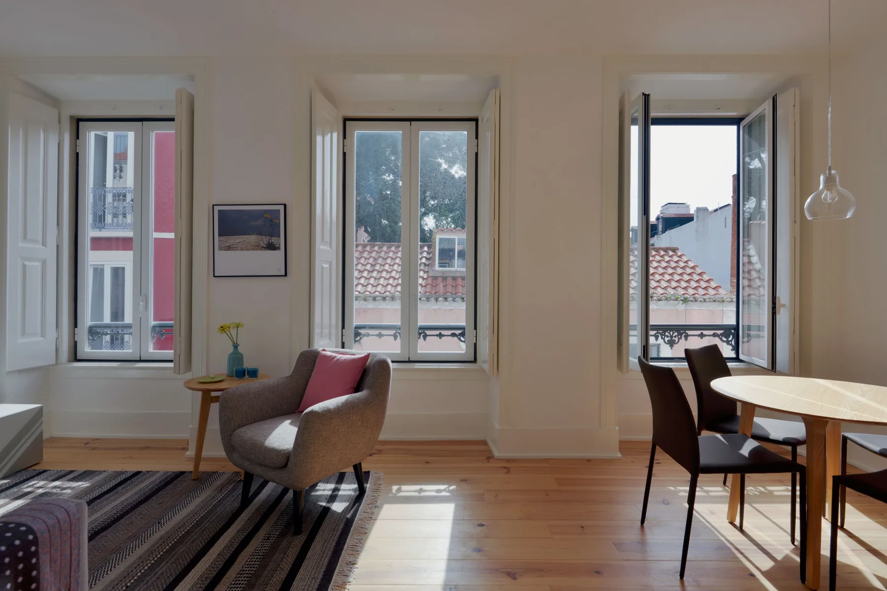 A bright living and dining area with windows, seating, and a wooden table.