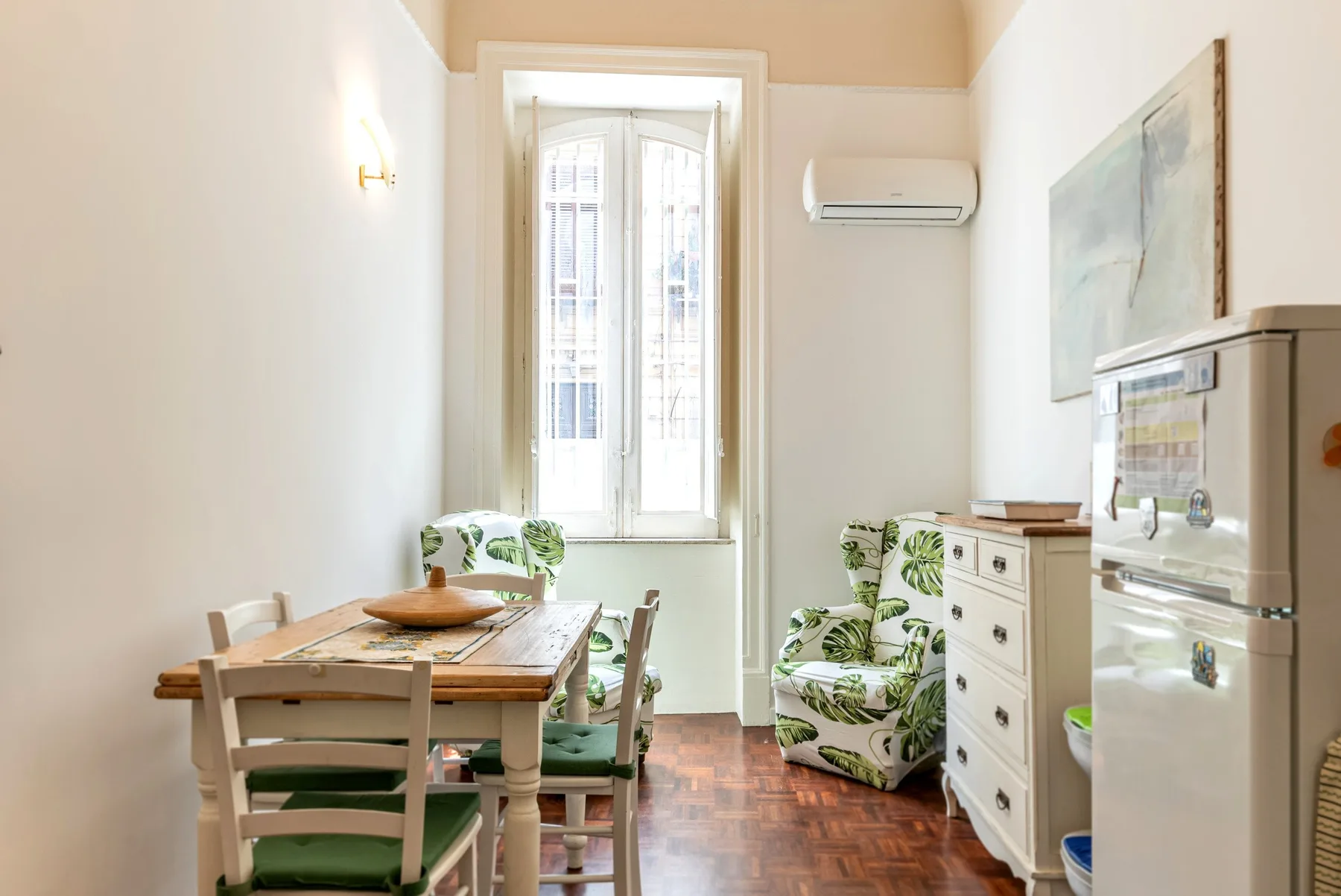 Un comedor luminoso con una mesa de madera y asientos estampados junto a una ventana alta.