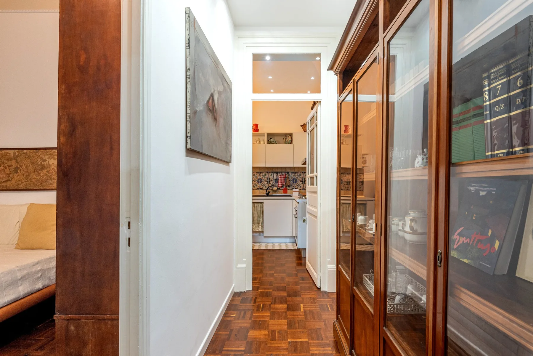 Un pasillo estrecho conduce a una cocina, con armarios de madera con puertas de vidrio a un lado.