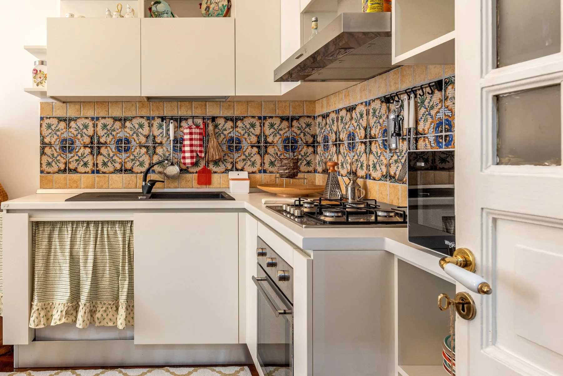 Una cocina compacta con gabinetes blancos, azulejos decorativos y una estufa de gas.
