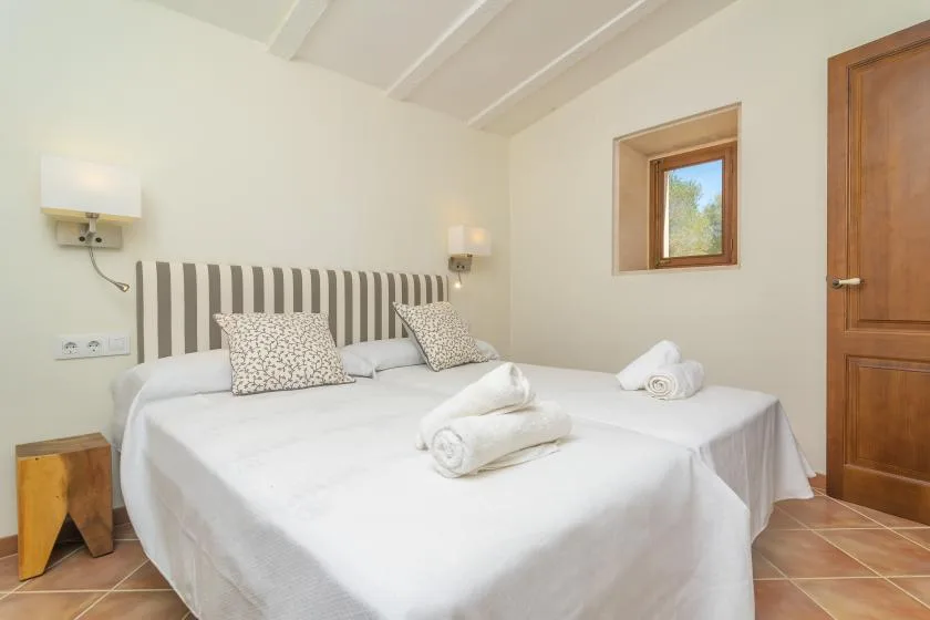 A bedroom with white bedding, striped headboards, and a small window.