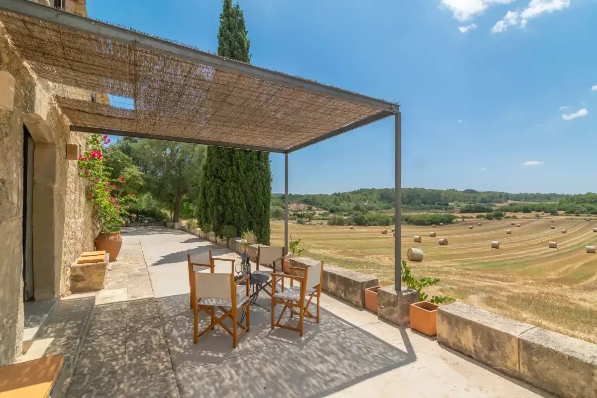 A stone terrace with outdoor seating overlooks open fields.