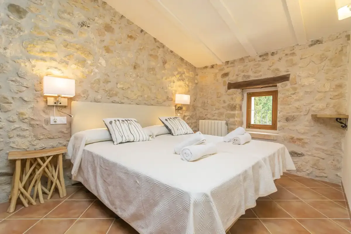 A bedroom with a large bed, white linens, and exposed stone walls.