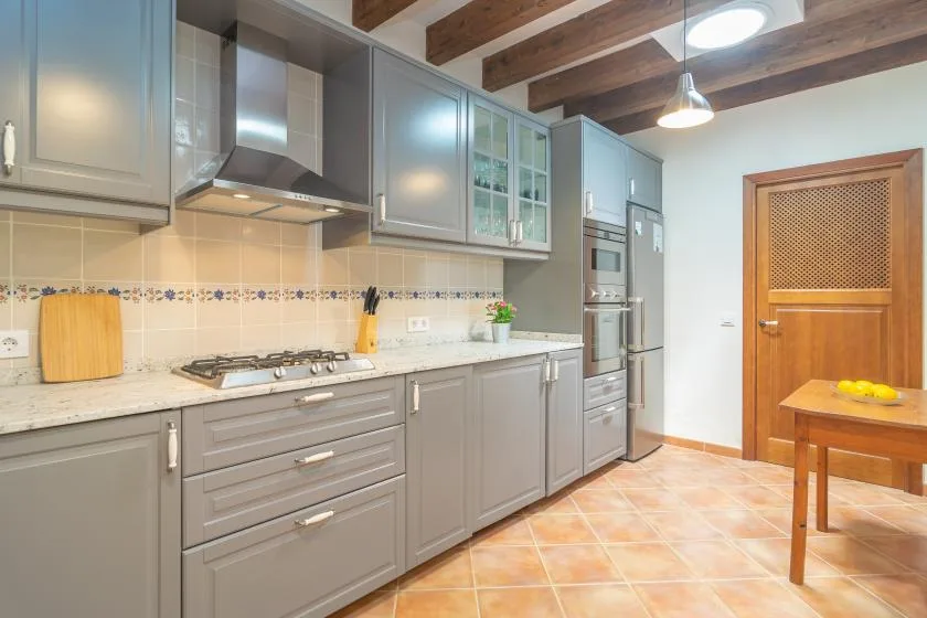 A modern kitchen with gray cabinets, a long countertop, and a wooden table.