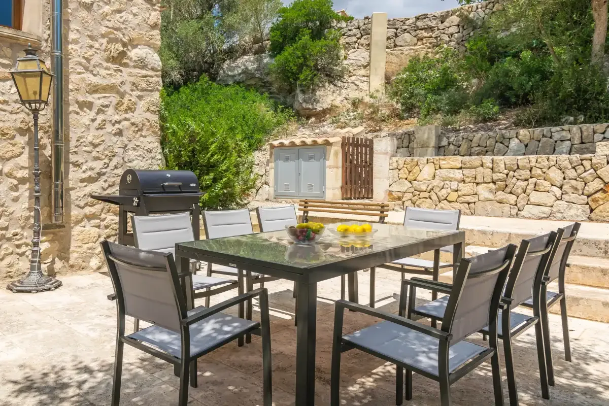An outdoor dining area with a table and seating beside stone walls and greenery.