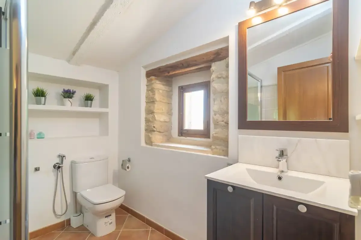 A bathroom with a sink, toilet, and a small window.