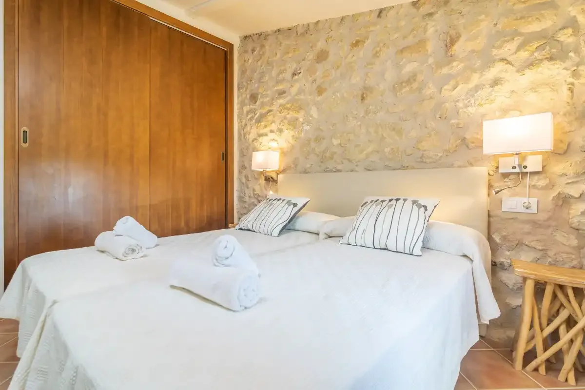A bedroom with a neatly made bed, striped pillows, and a stone wall.