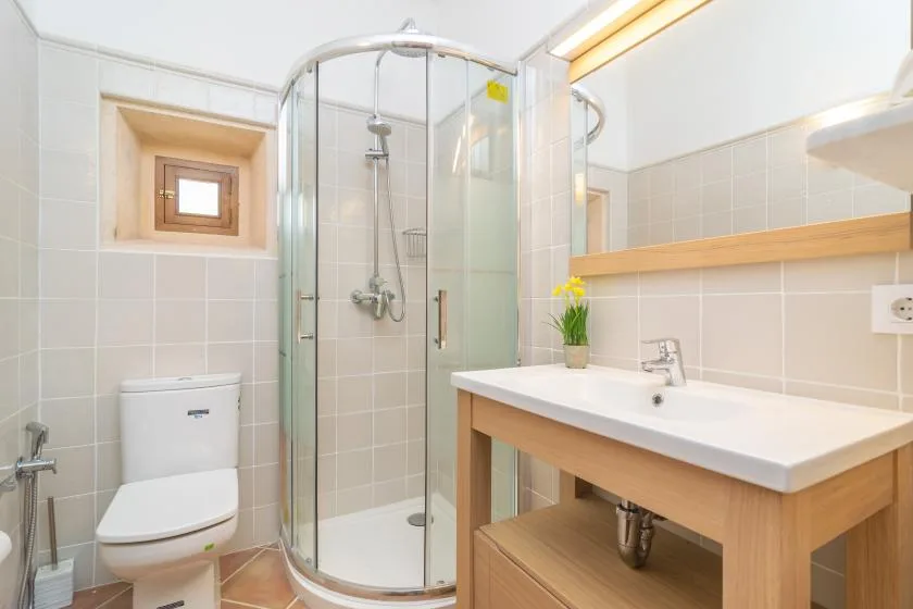 A tiled bathroom with a curved glass shower, toilet, and wooden vanity.