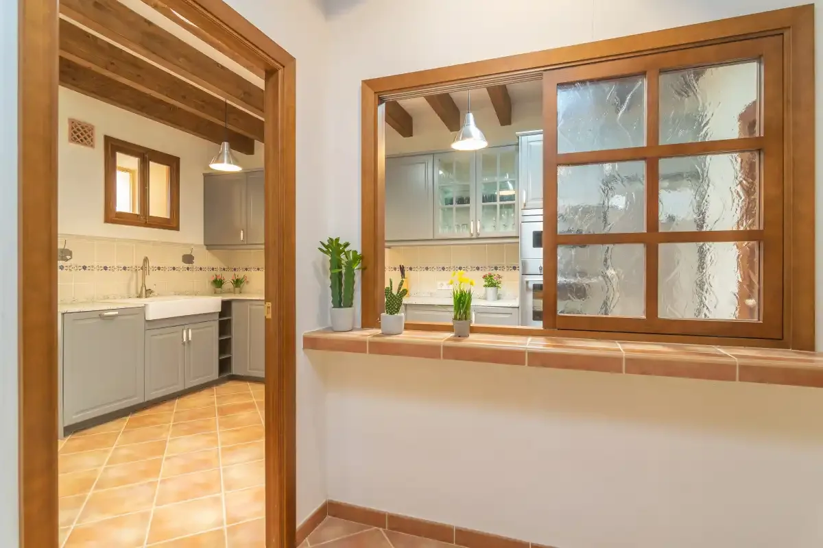 A kitchen is visible through an interior opening beside a wooden-framed window.