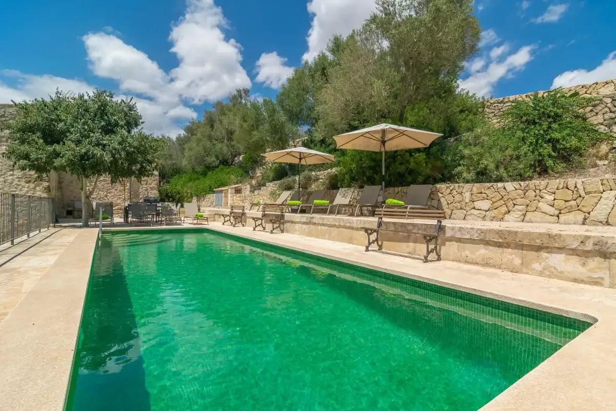An outdoor swimming pool beside stone walls and shaded seating.