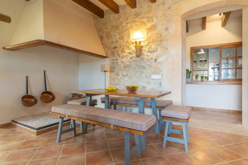 A rustic dining area with a long table, benches, and a stone wall.