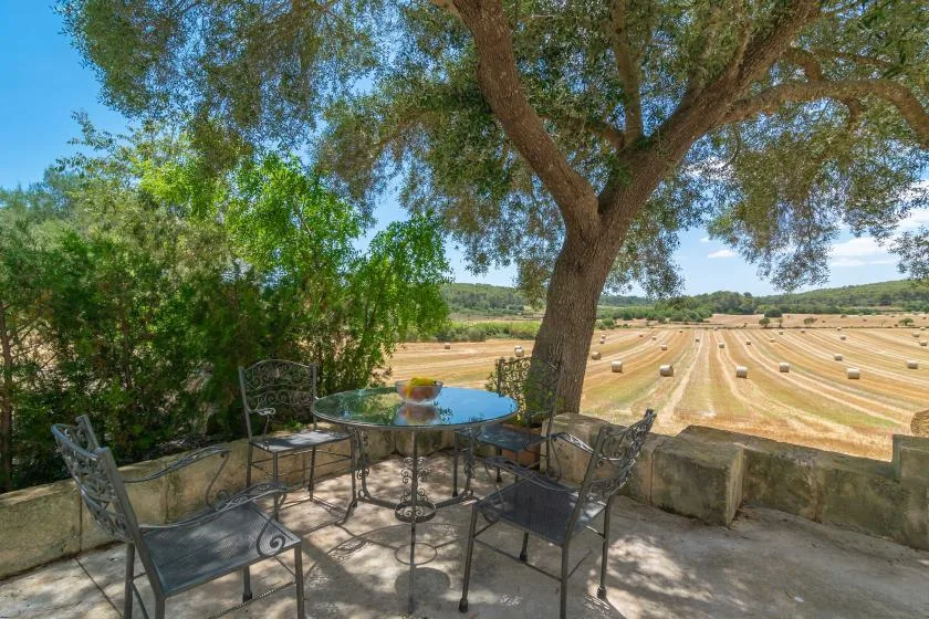 A shaded outdoor seating area overlooks a field with hay bales.