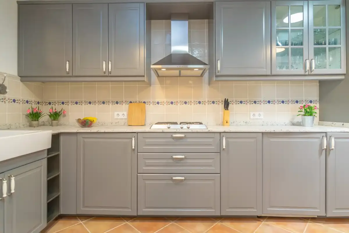 A kitchen with gray cabinets, a tiled backsplash, and a countertop.