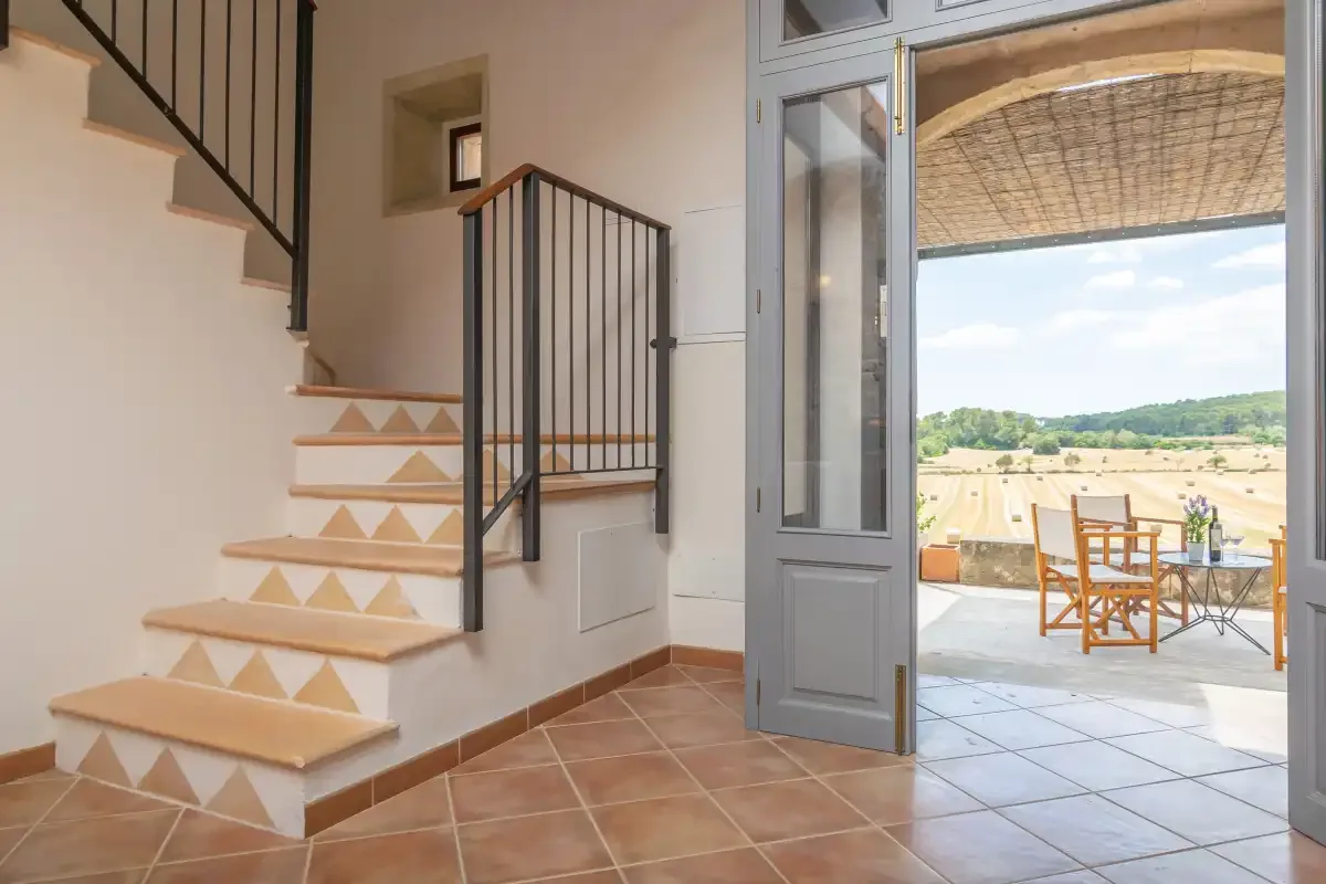 An interior staircase opens onto a patio with outdoor seating and a countryside view.