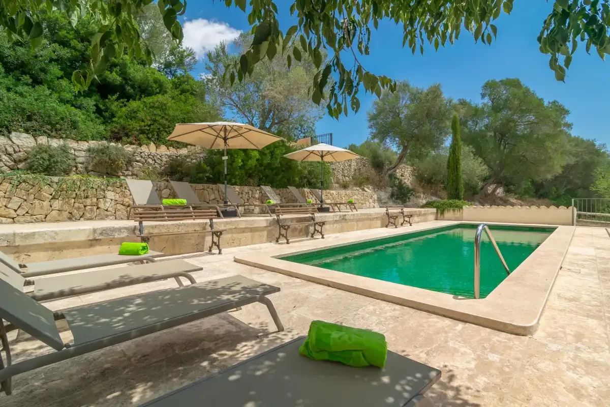 An outdoor swimming pool is surrounded by sun loungers, umbrellas, and greenery.