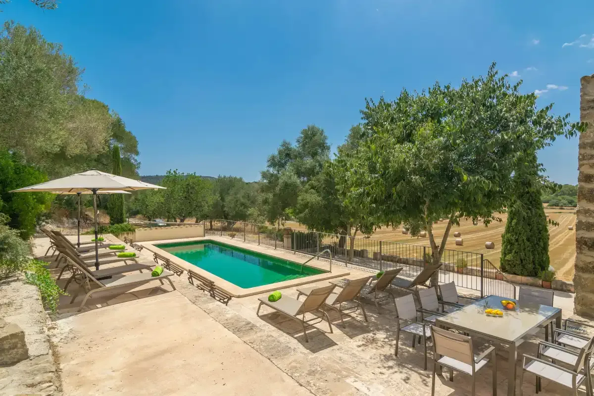 A swimming pool and patio seating sit beside a fenced garden.