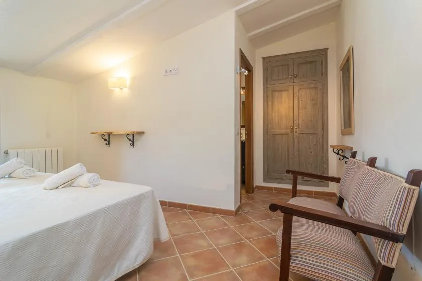 A bedroom with a neatly made bed and striped seating beside the doorway.
