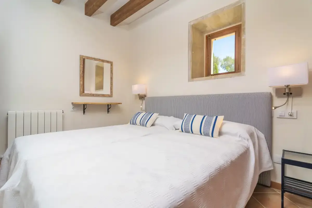 A bedroom with a large bed, striped pillows, and exposed ceiling beams.